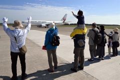 滑走路脇で旅客機へ手を振るお見送り体験の参加者（須貝拓也撮影）