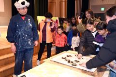 バレンを手に版画の仕上げ作業に挑戦する来場者と石村さん(左)