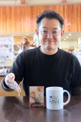 アクリルキーホルダーとマグカップをＰＲする菅原店長