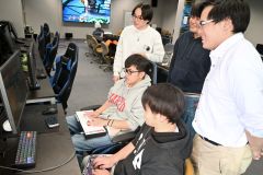 ゲーミングＰＣ室で活動するｅスポーツ部の部員たちと薦田専任講師（右）