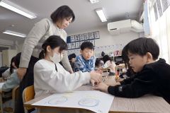 杉山代表（上）の説明を聞き、やさしい日本語に挑戦する児童たち