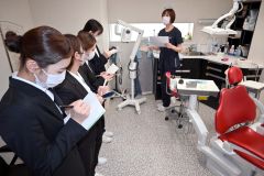 歯科衛生士（右）から設備の説明を受け、メモを取る学生（２０２５年５月１９日、帯広市内の歯科医院で）