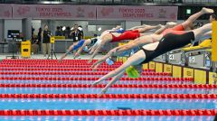 合図とともに一斉に飛び込む競泳選手たち。機器(左奥など)に点滅する白、赤、青の色変化によって選手にスタートを知らせる(20日、東京アクアティクスセンター)