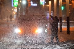 車に降り積もった雪を落とすドライバー(14日午後6時ごろ、帯広駅北口で。塩原真撮影)