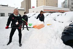 職場の雪をスコップで除雪する従業員(15日午前7時20分ごろ、帯広市西1南12。塩原真撮影)