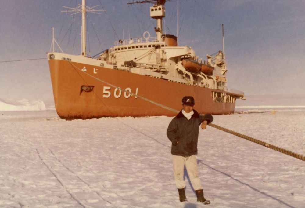 南極観測船「ふじ」をバックにして写真に納まる佐藤さん