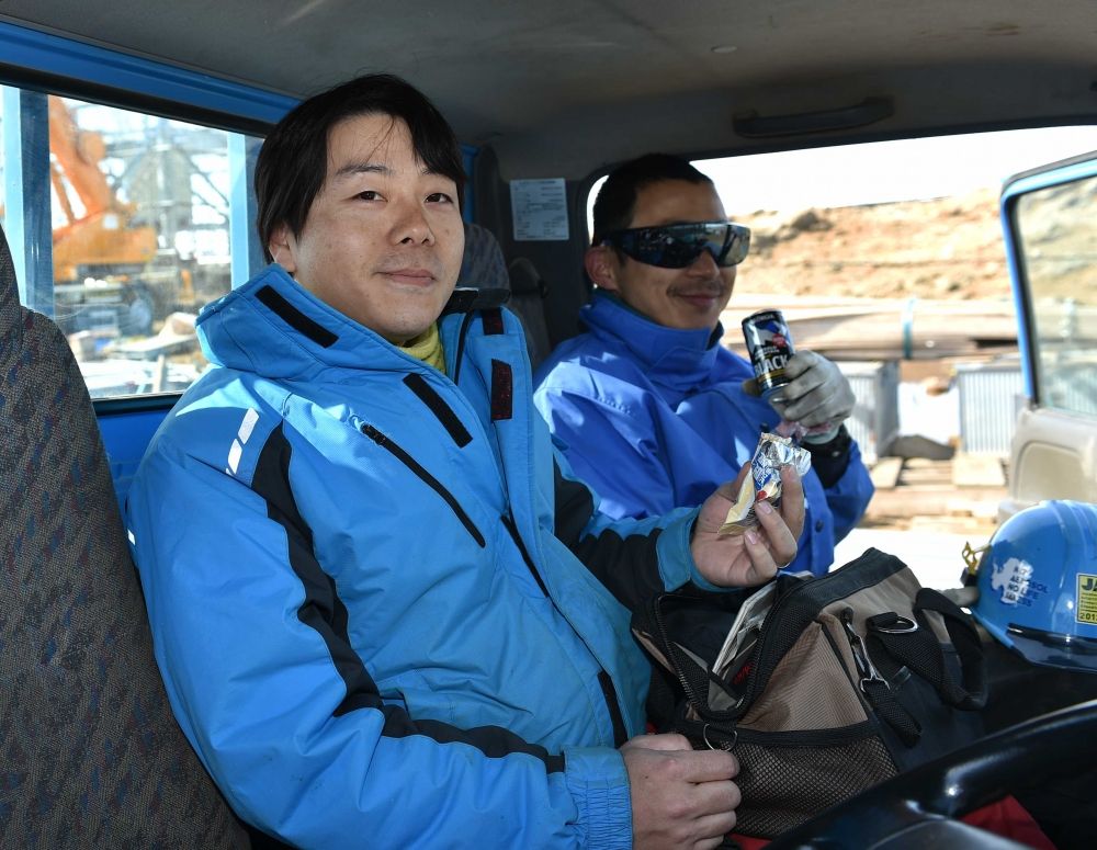 休憩中にトラックの中でおやつを頬張る久保田寛丈隊員と同行者の須藤健司さん（左から）