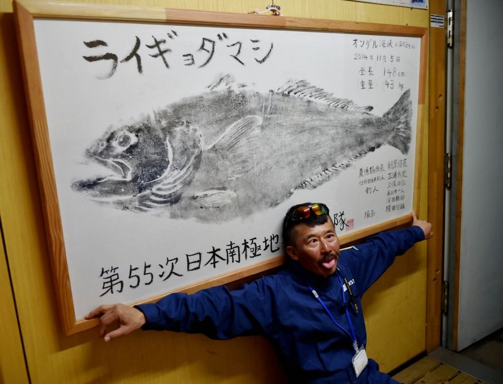 昭和基地の管理棟に飾られているライギョダマシの魚拓と一緒に写る小林隊員